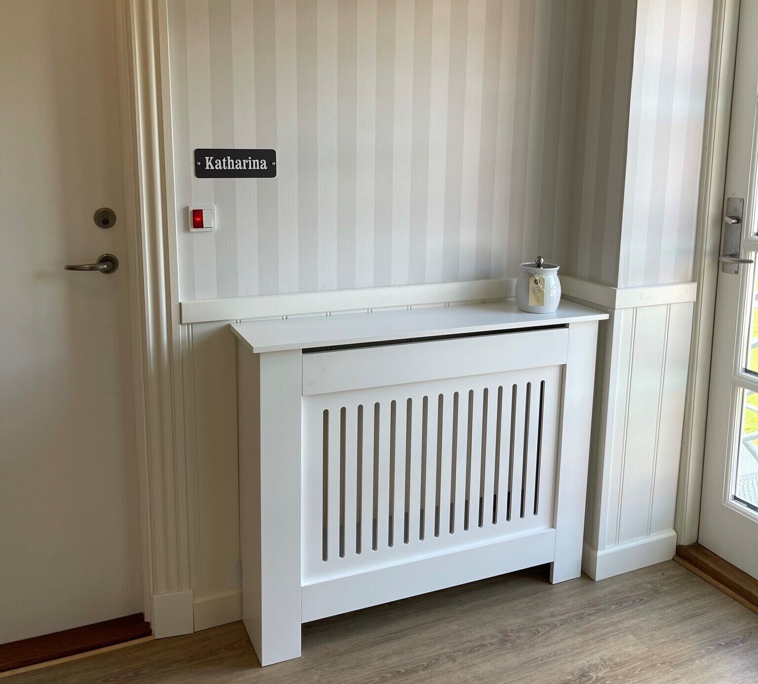 A white door with a nameplate reading "Katharina" and a small white radiator below it.