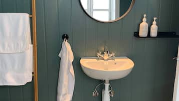 Un baño con un lavamanos blanco, un espejo redondo, una escalera de madera, una bañera blanca y una cesta de mimbre.