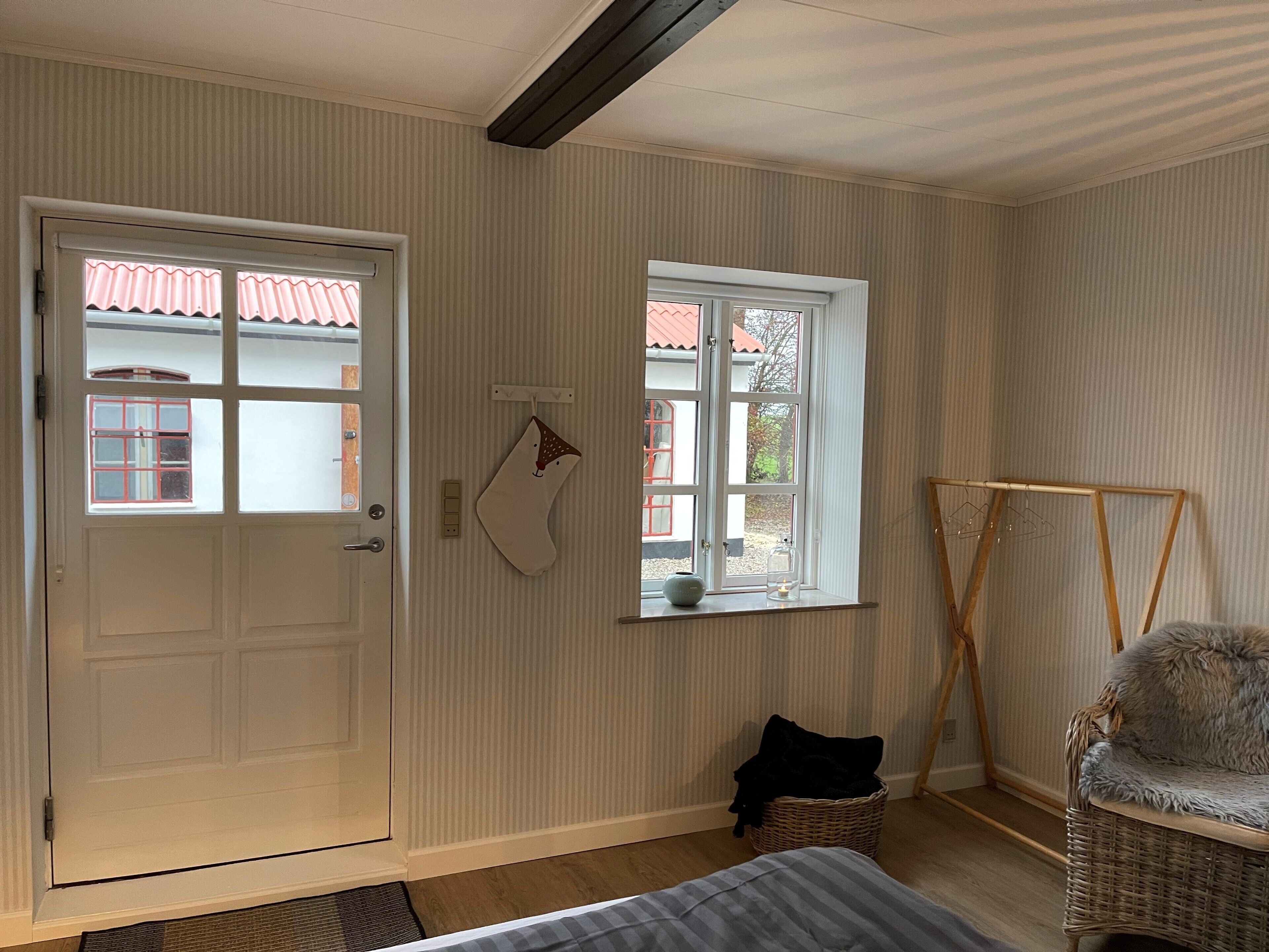 Een kamer met een bed, een rieten stoel, een raam met uitzicht, een deur en een klein mandje.