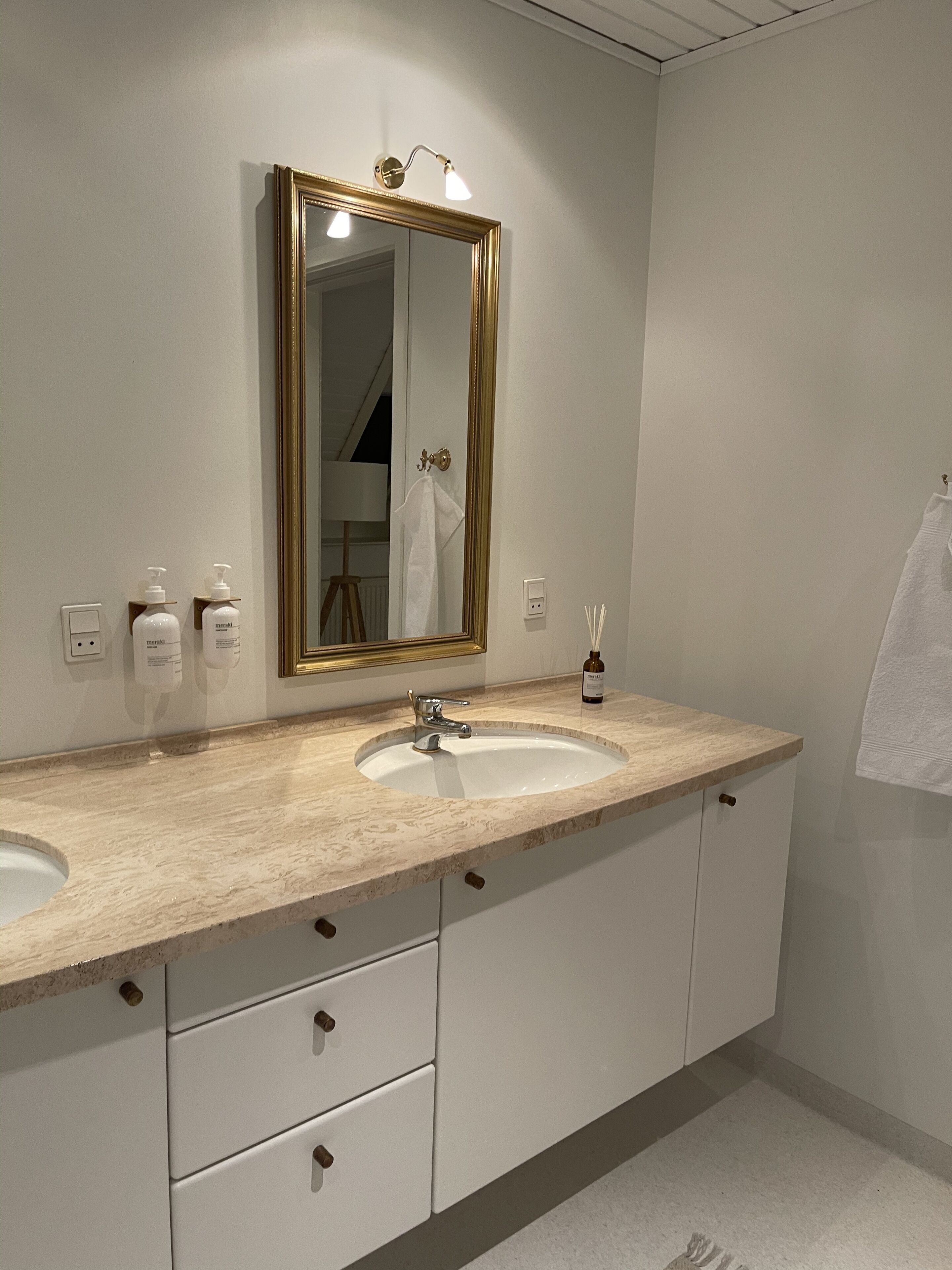 A bathroom with two sinks, a large mirror with lights, and a towel hanging on the wall.