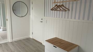 Een kamer met een houten vloer, een witte garderobe met twee lades, een spiegel en een gestreepte wand.