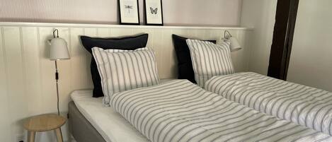 A neatly made bed with striped bedding, a bedside lamp, and a small wooden stool.