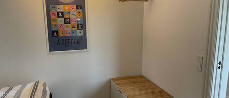 Un dormitorio con cama, un pequeño armario blanco, una lámpara colgante y un cartel en la pared.