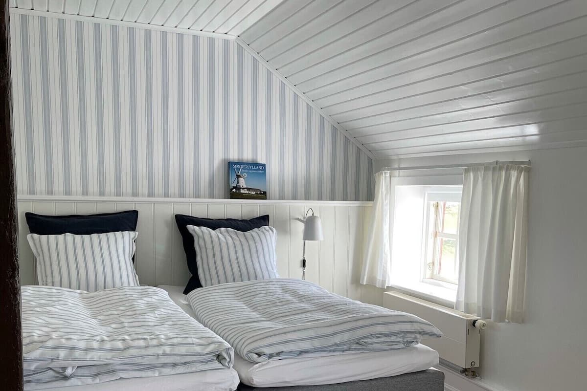 Una habitación con dos camas, ropa de cama a rayas, un libro en la pared y una ventana con cortinas.