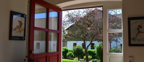 Puerta abierta que da a un jardín con un edificio blanco y un árbol de flores rosadas.