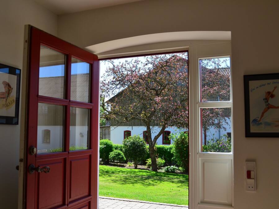 An open door leading to a garden with a white building and a tree with pink blossoms.