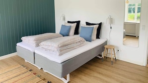 Un dormitorio moderno con una cama gris, ropa de cama a rayas, un taburete pequeño, un espejo y una pared verde.
