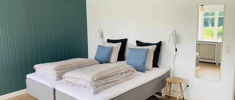 Un dormitorio moderno con una cama gris, ropa de cama a rayas, un taburete pequeño, un espejo y una pared verde.