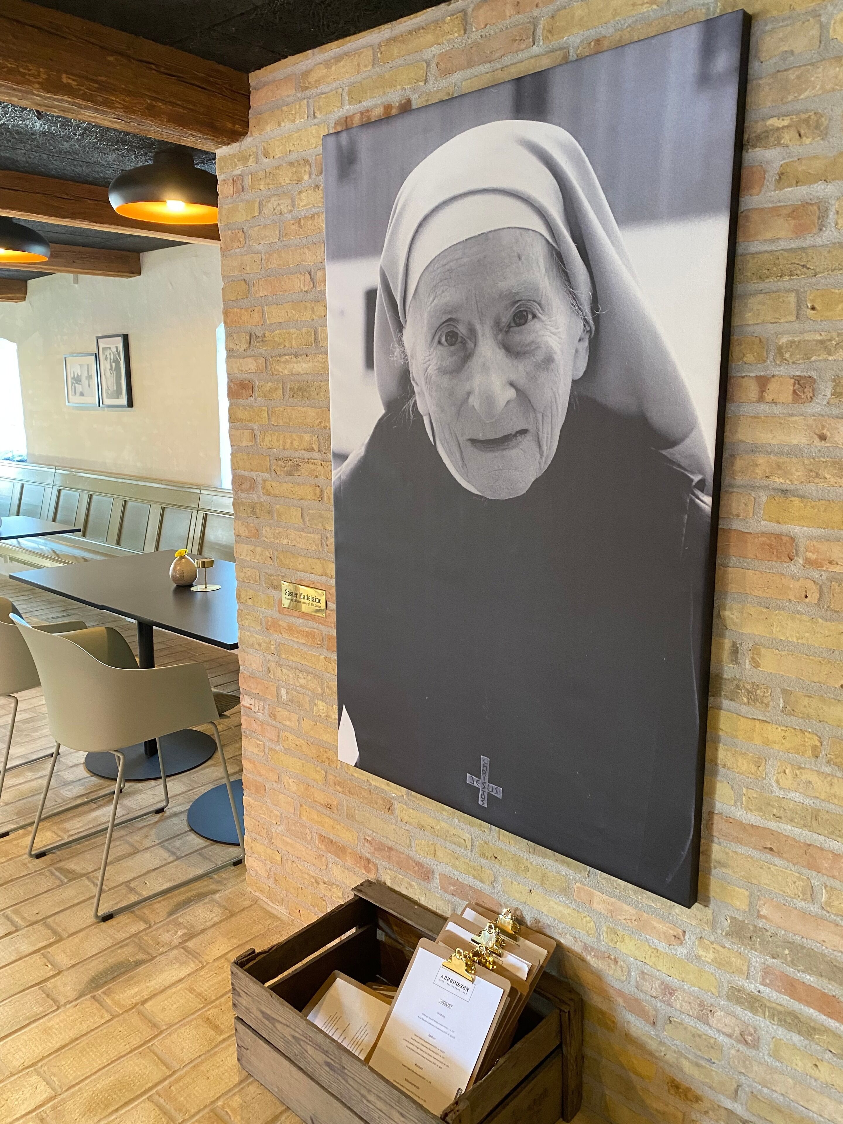 A dining area with a brick wall, wooden beams, and a large framed photograph.