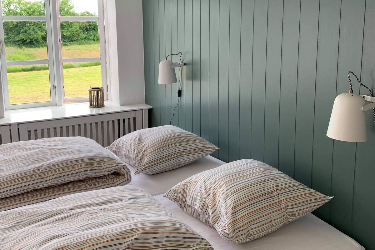 Un dormitorio con dos camas, una ventana con vistas a zonas verdes y una lámpara fijada a la pared.