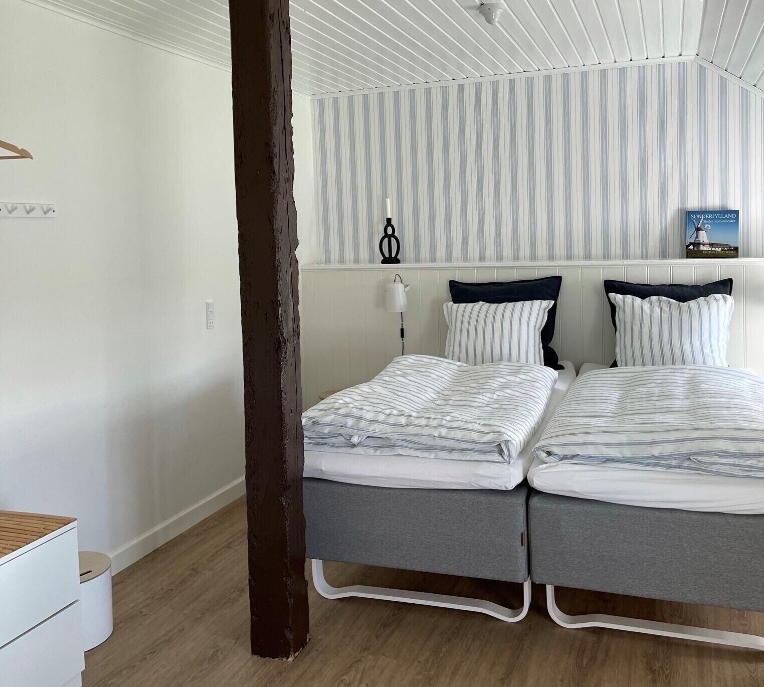 A double bed with striped bedding in a room with wooden flooring and a striped wall panel.