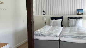 A double bed with striped bedding in a room with wooden flooring and a striped wall panel.