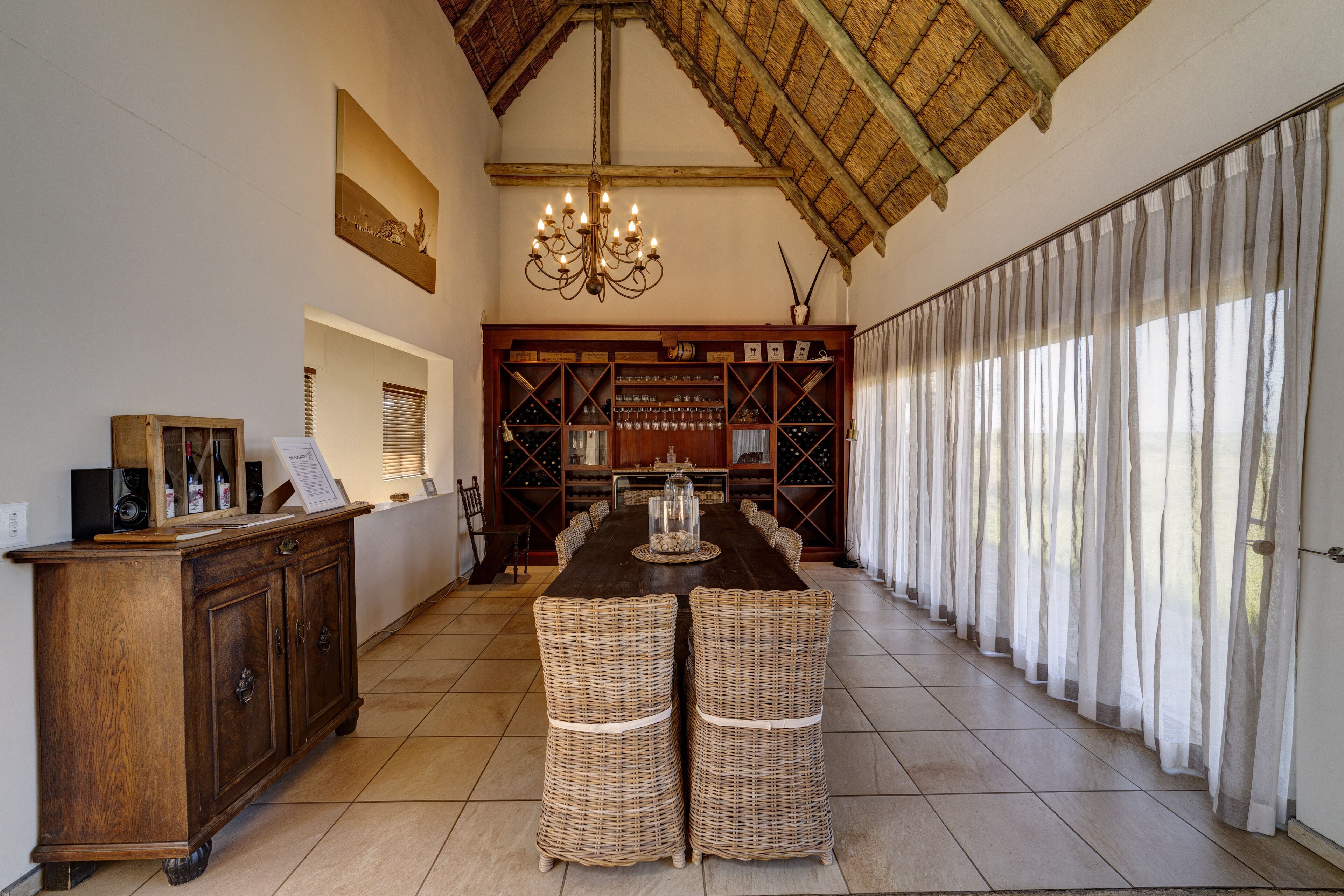 A dining area with a long table, wicker chairs, a wooden cabinet, and a chandelier.