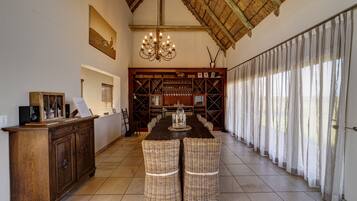 A dining area with a long table, wicker chairs, a wooden cabinet, and a chandelier.