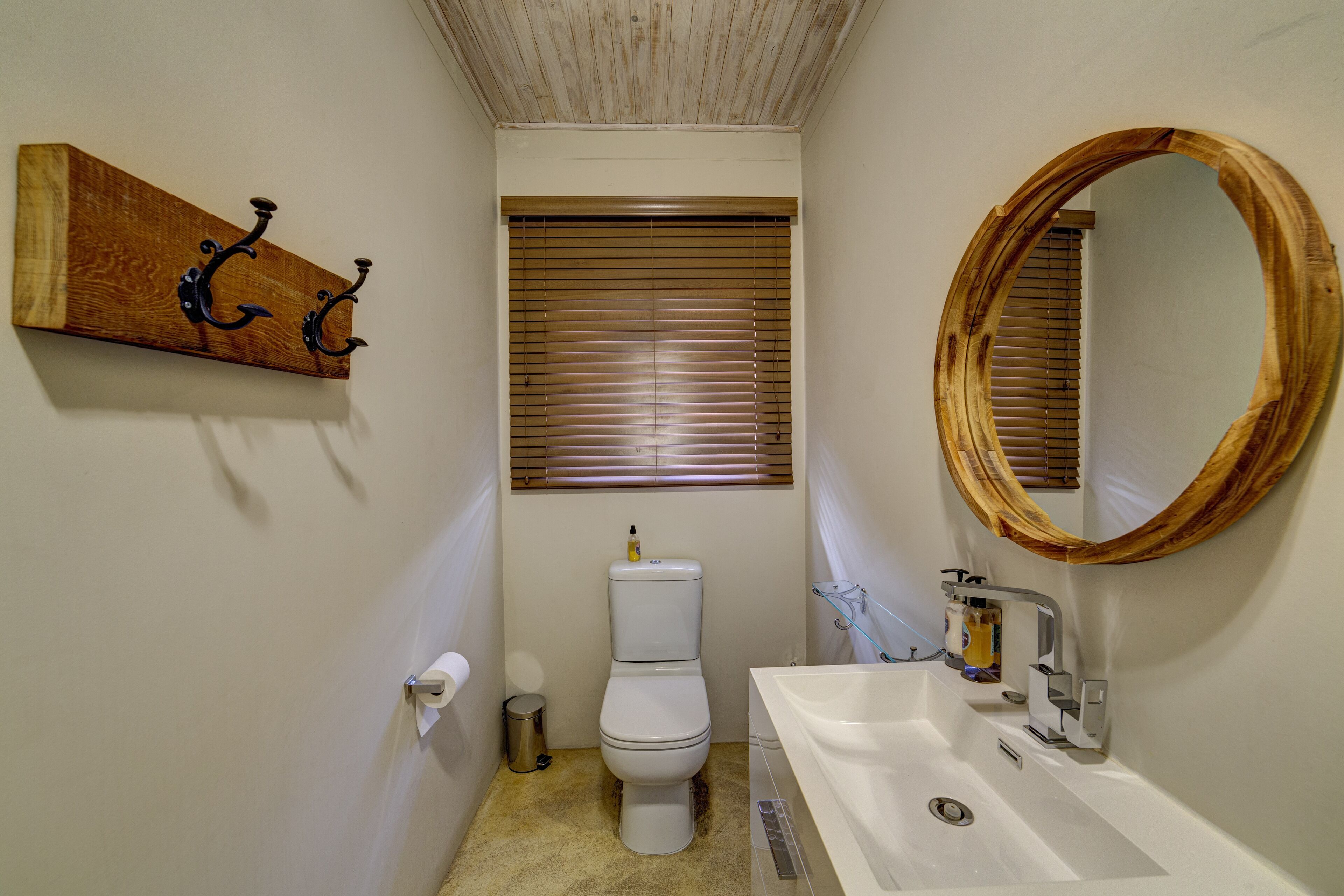 A small bathroom with a toilet, sink, and wooden shelf with hooks.