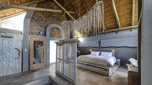 Une chambre à coucher avec un lit, un banc en bois, une chaise blanche, un mur en pierre, une porte en bois et un luminaire suspendu.