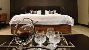Una habitación de hotel con una cama grande, una mesita de noche con copas de vino y una silla.
