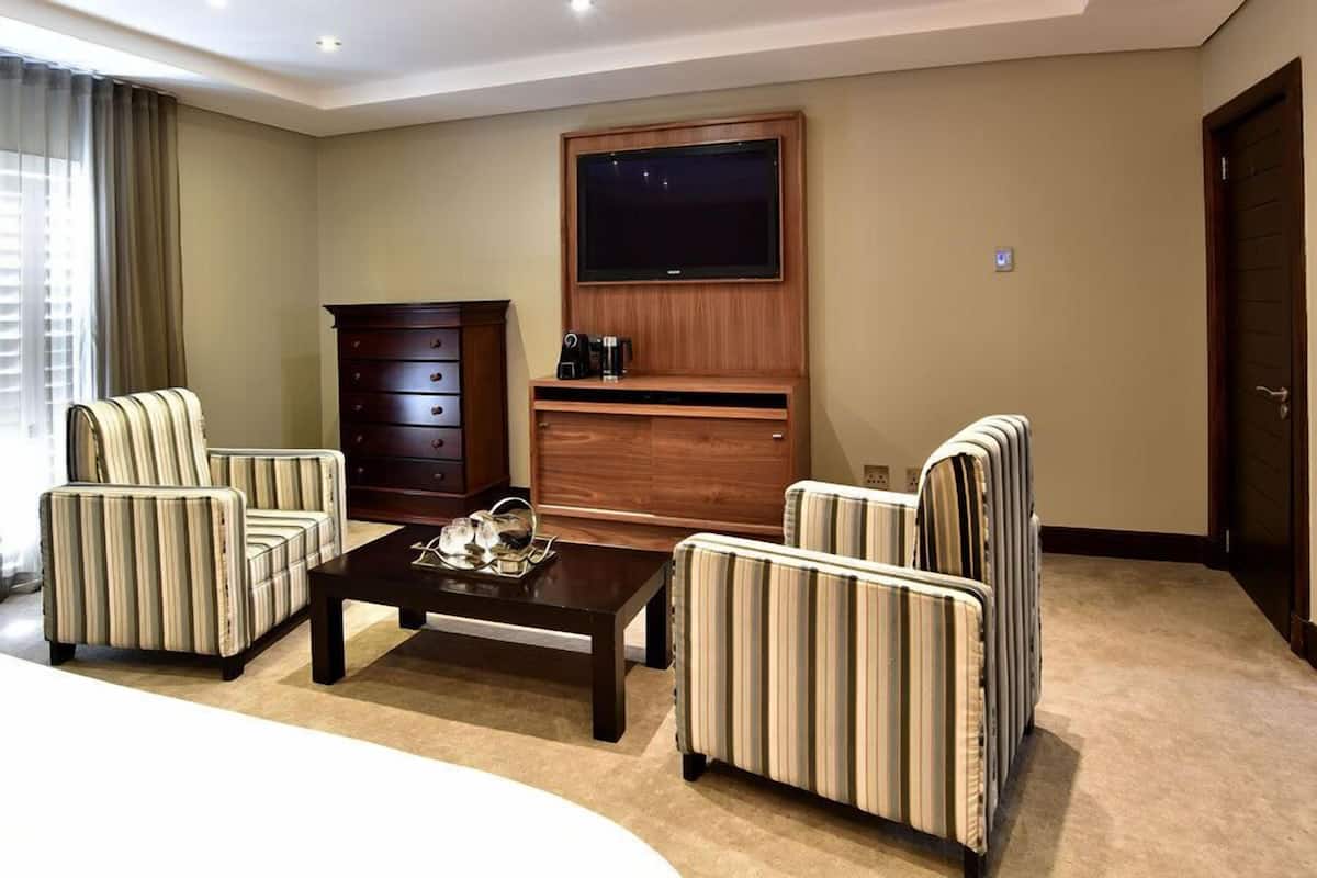 Ein Hotelzimmer mit gestreifte Sesseln, einem Holzschrank, einem Flachbildfernseher und einer Kaffeemaschine.