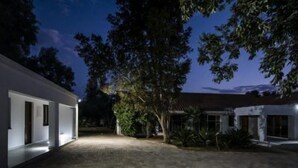 A modern house with a paved courtyard, large trees, and a well-lit exterior. - The Royal Guest House (Klerksdorp)