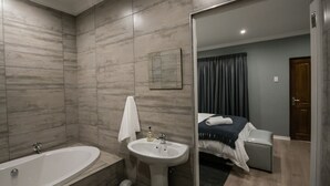 A modern bathroom with a bathtub, sink, and mirror. - The Royal Guest House (Klerksdorp)