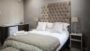 A modern hotel room with a large bed, a bedside table, a desk with a lamp, and a wardrobe. - The Royal Guest House (Klerksdorp)