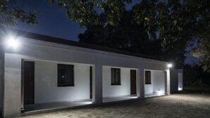 A modern building with a series of rooms, each with a door and a window, illuminated by exterior lighting. - The Royal Guest House (Klerksdorp)