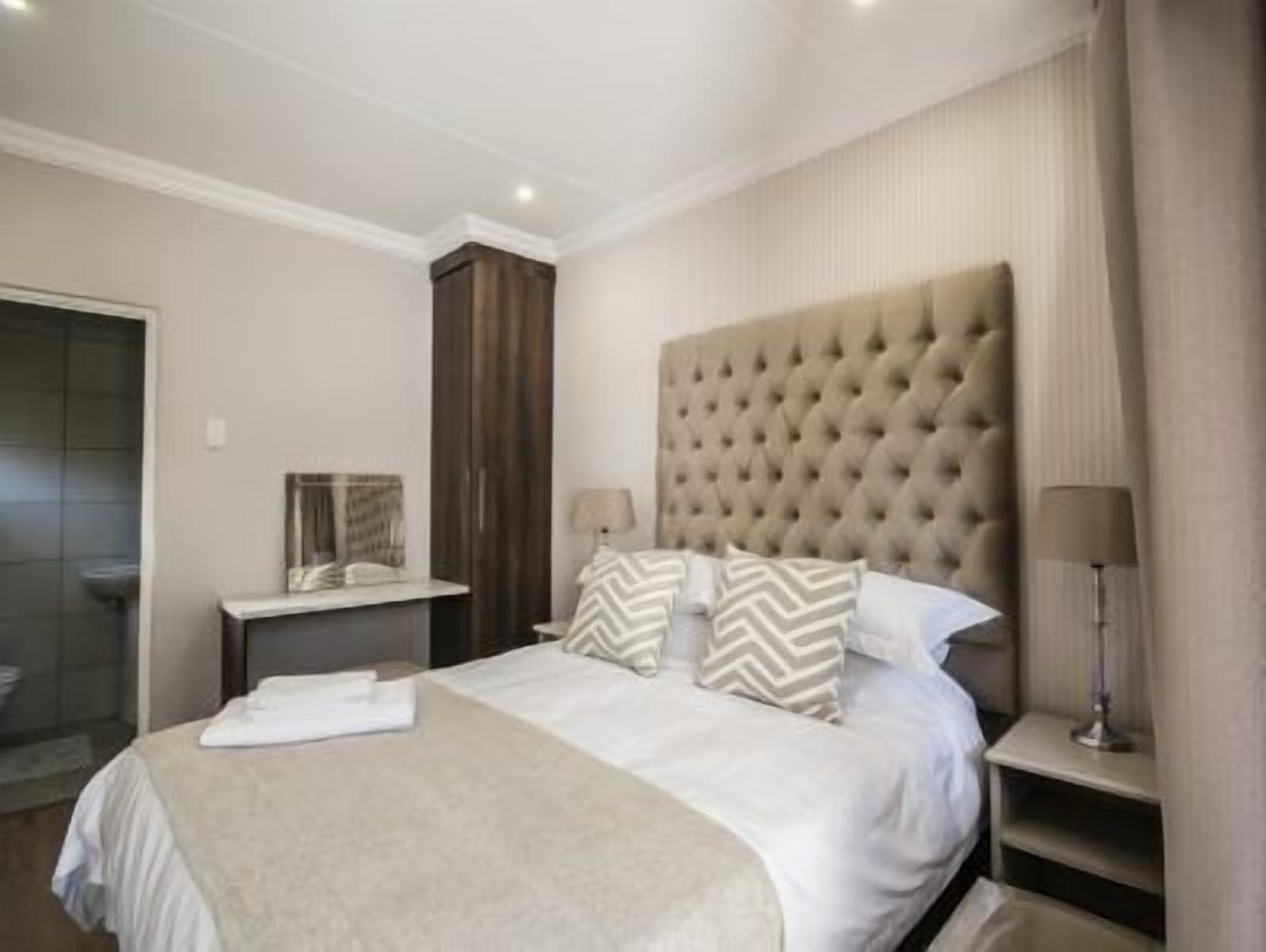A hotel room with a large bed, a bedside table with a lamp, a mirror, and a wardrobe.