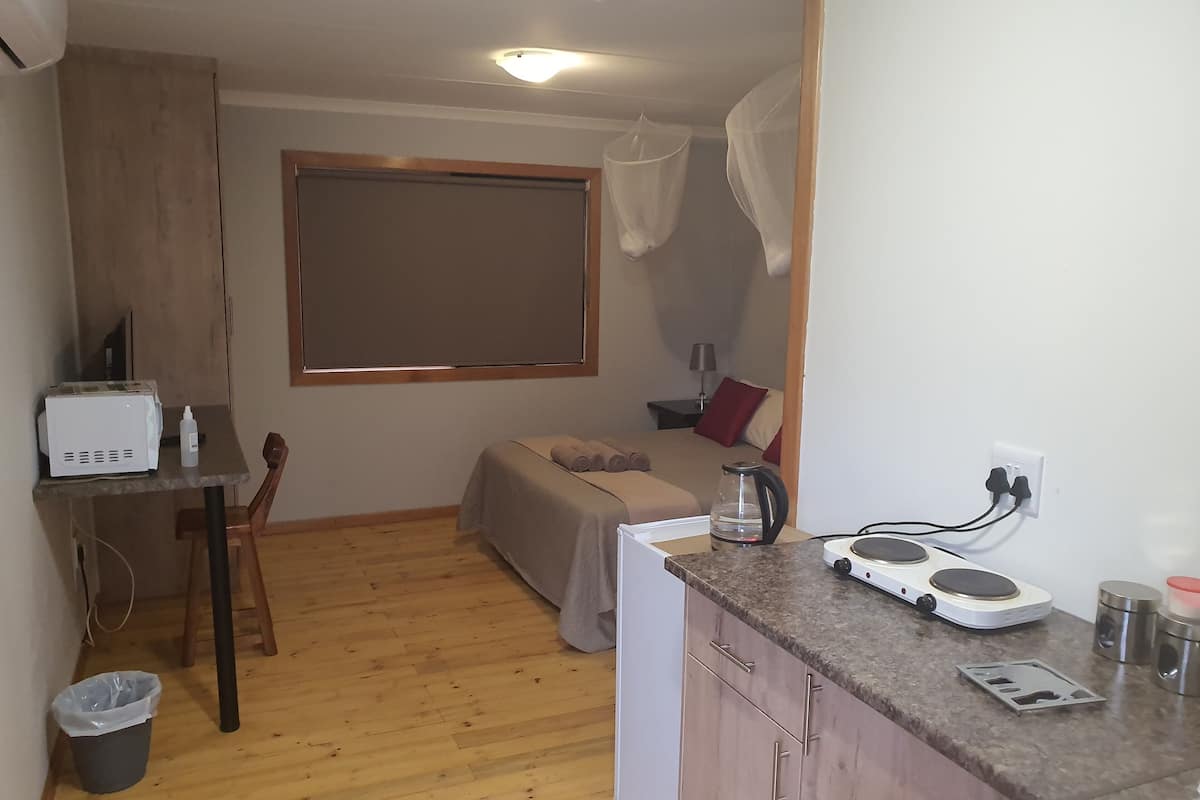 A compact room with a kitchenette, a bed with a canopy, a small table, and a trash bin.