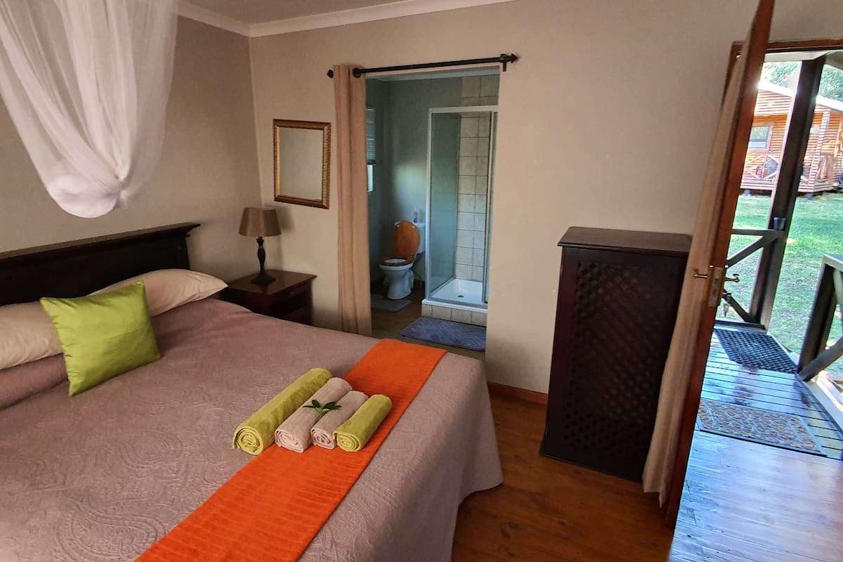 A hotel room with a bed, a nightstand, a mirror, a bathroom visible through an open door, and a balcony.