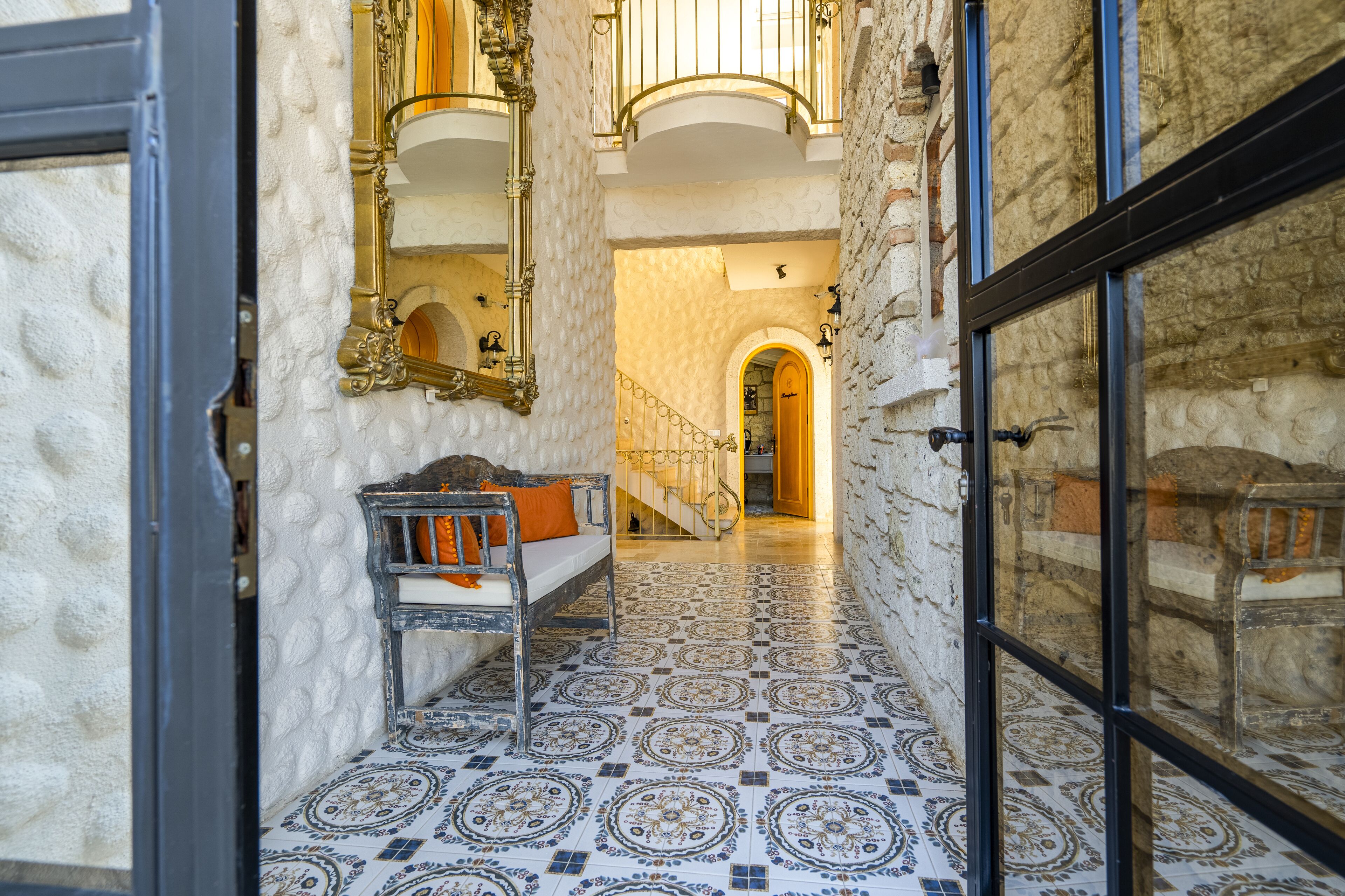 A narrow hallway with patterned tile flooring, a bench with cushions, and a staircase leading to an upper level.