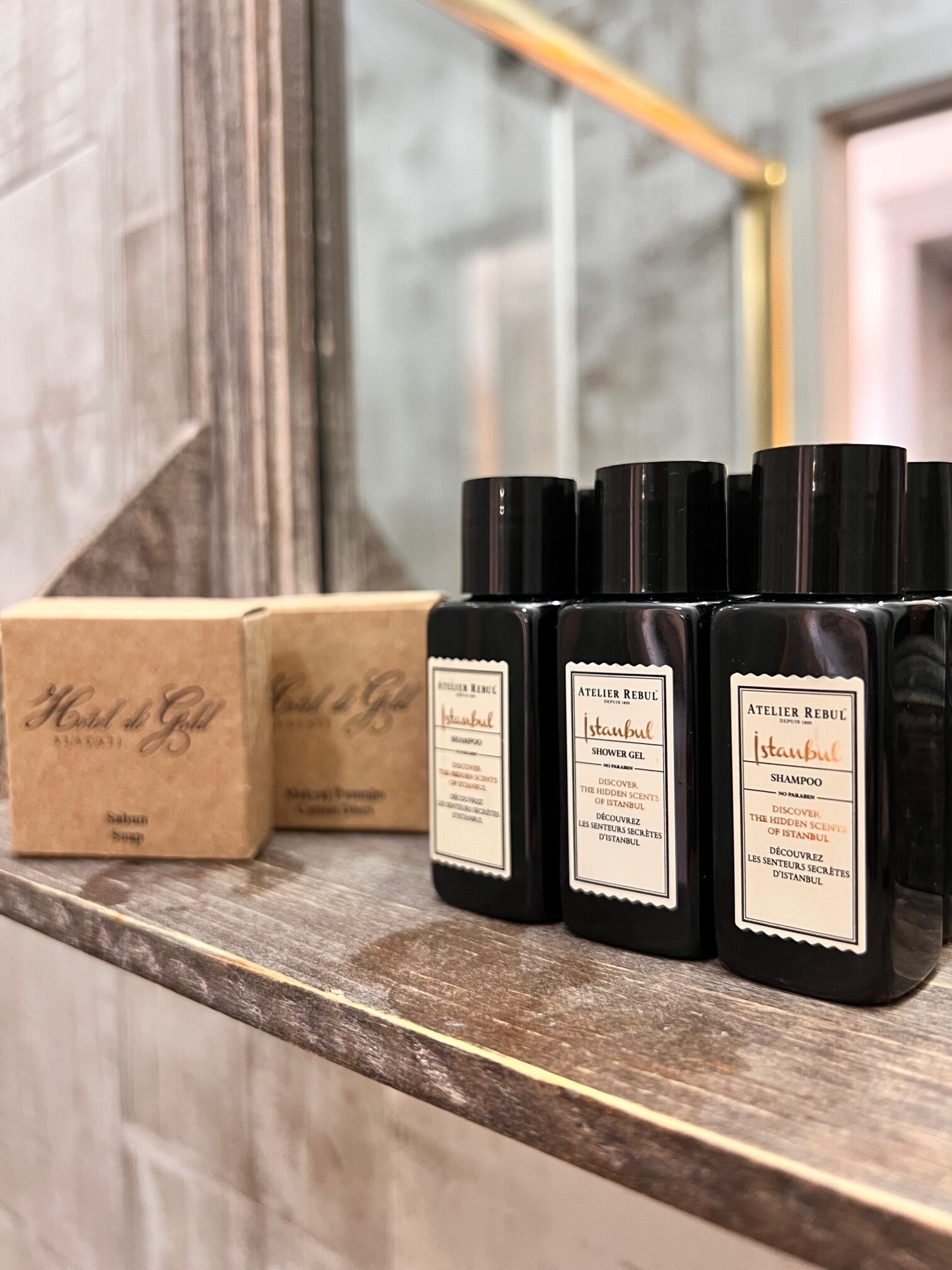 A bathroom shelf with four black bottles of Istanbul shower gel and a brown box of Hotel de Gold soap.