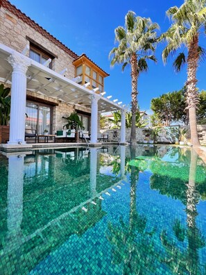 A clear pool with a stone building and palm trees in the background. - Hotel De Gold Alacati (Cesme)