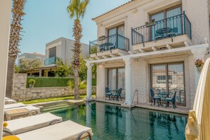 A pool area with lounge chairs and a table, surrounded by a building with balconies and a stone wall. - Hotel De Gold Alacati (Cesme)