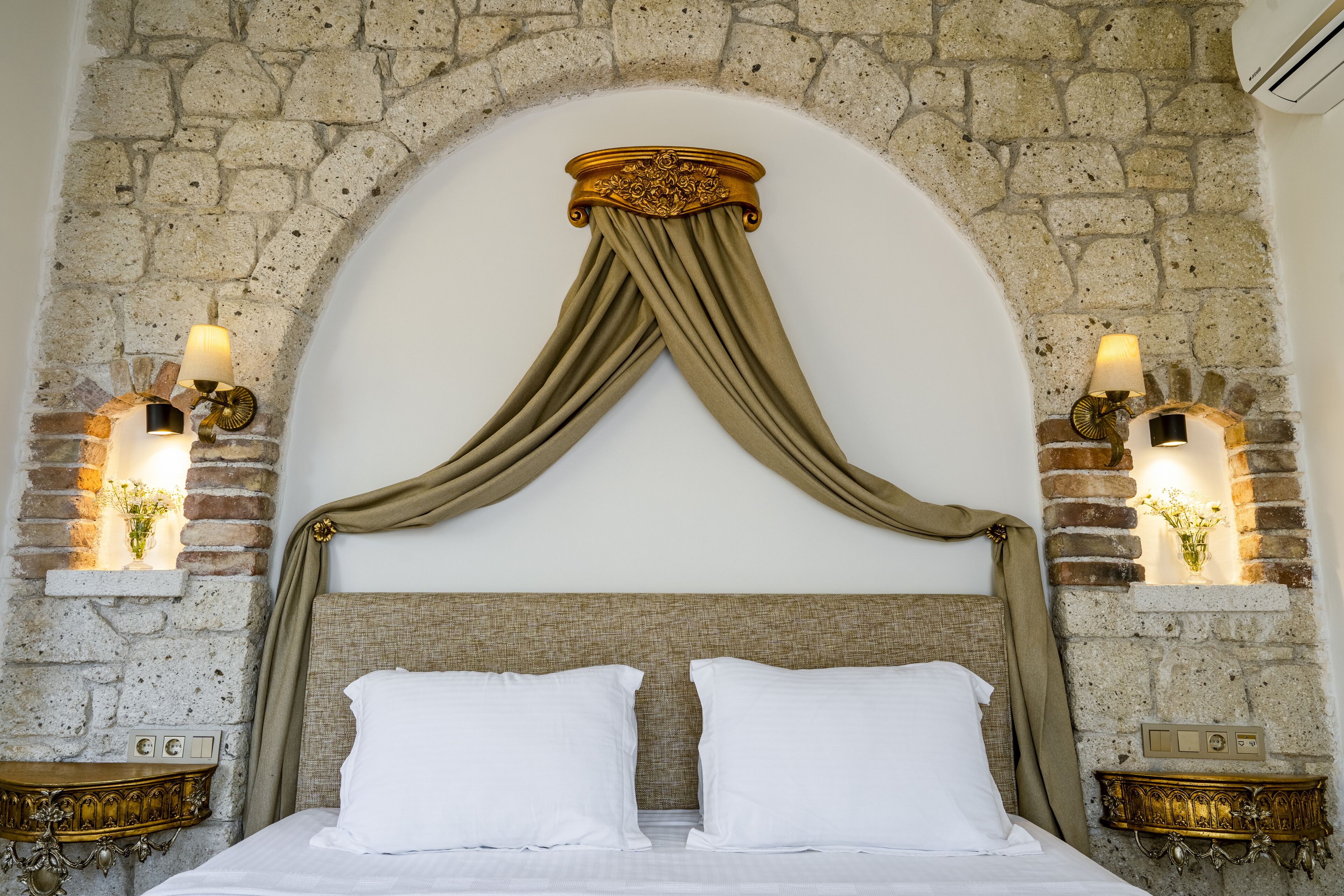 A bed with a stone wall backdrop, a draped canopy, and two wall-mounted lamps.