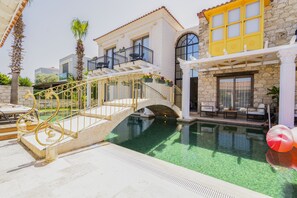 A pool area with a bridge, stone buildings, and outdoor furniture. - Hotel De Gold Alacati (Cesme)