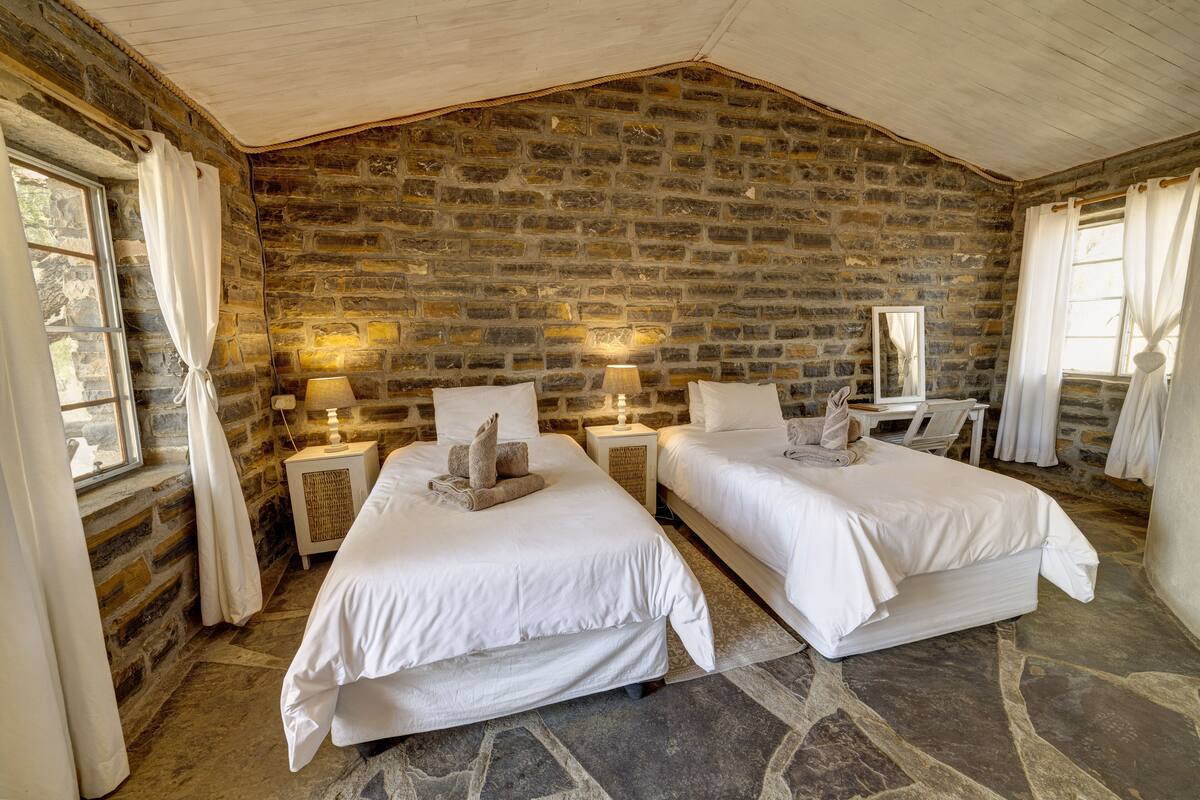 Una habitación con dos camas, paredes de piedra y techo de madera rústica.