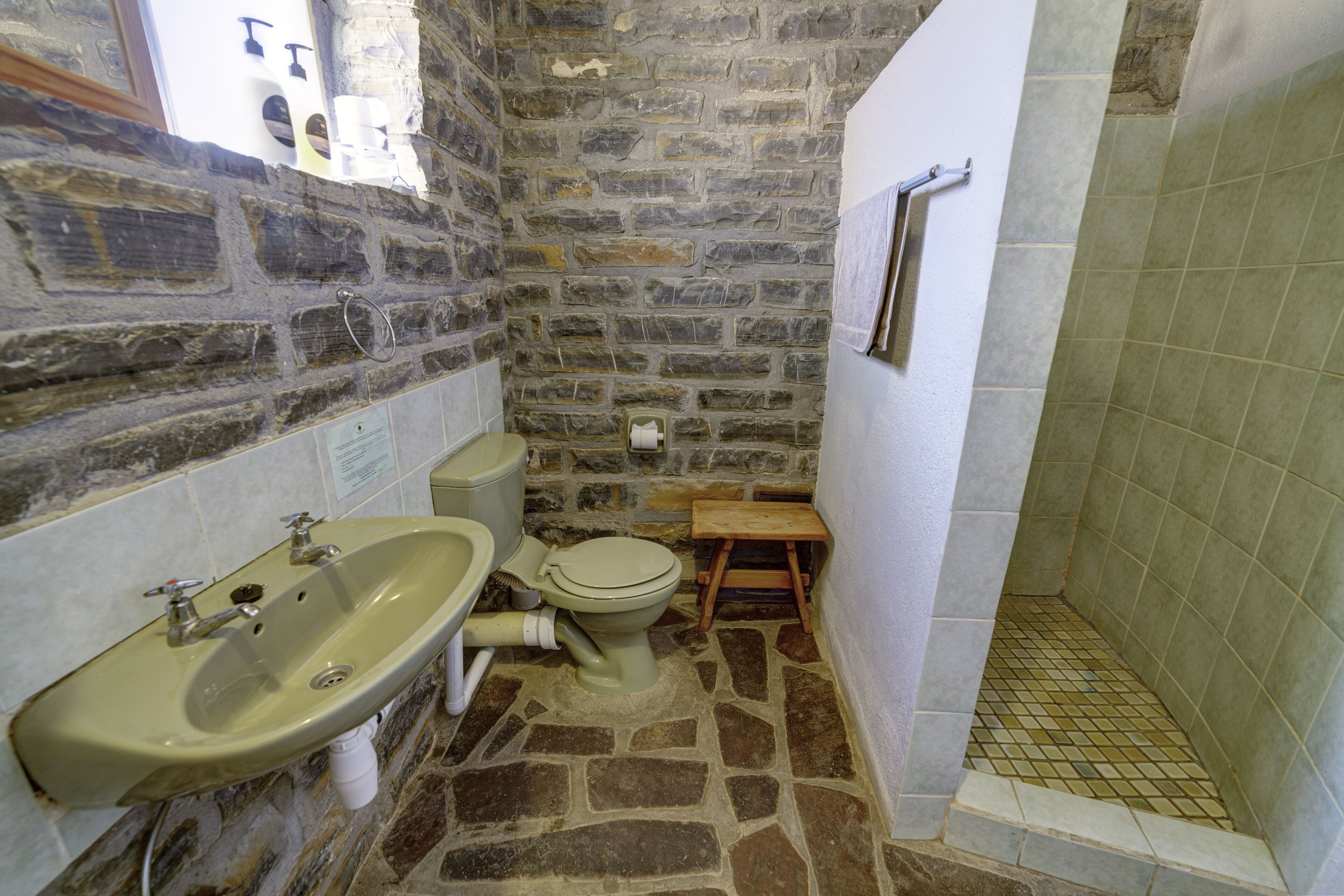 A bathroom with a stone wall, a sink, a toilet, and a shower area.