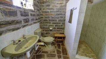 A bathroom with a stone wall, a sink, a toilet, and a shower area.