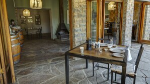 A stone-floored dining area with a wooden table set for four, surrounded by stone walls and wooden beams. - Neuras Wine & Wildlife Estate (Sesriem)
