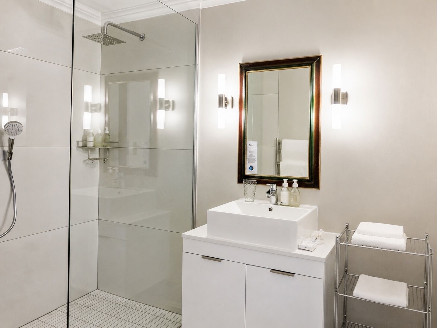 A modern bathroom with a glass-enclosed shower, a white sink with a mirror, and a towel rack.