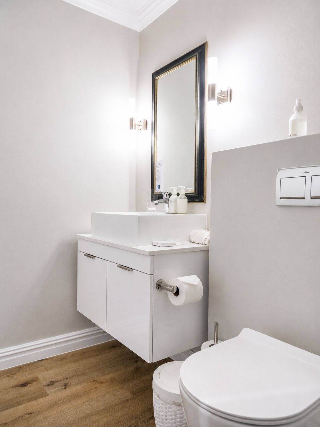 Une salle de bain moderne avec un meuble-lavabo blanc, des toilettes et un miroir doté d’un cadre doré.