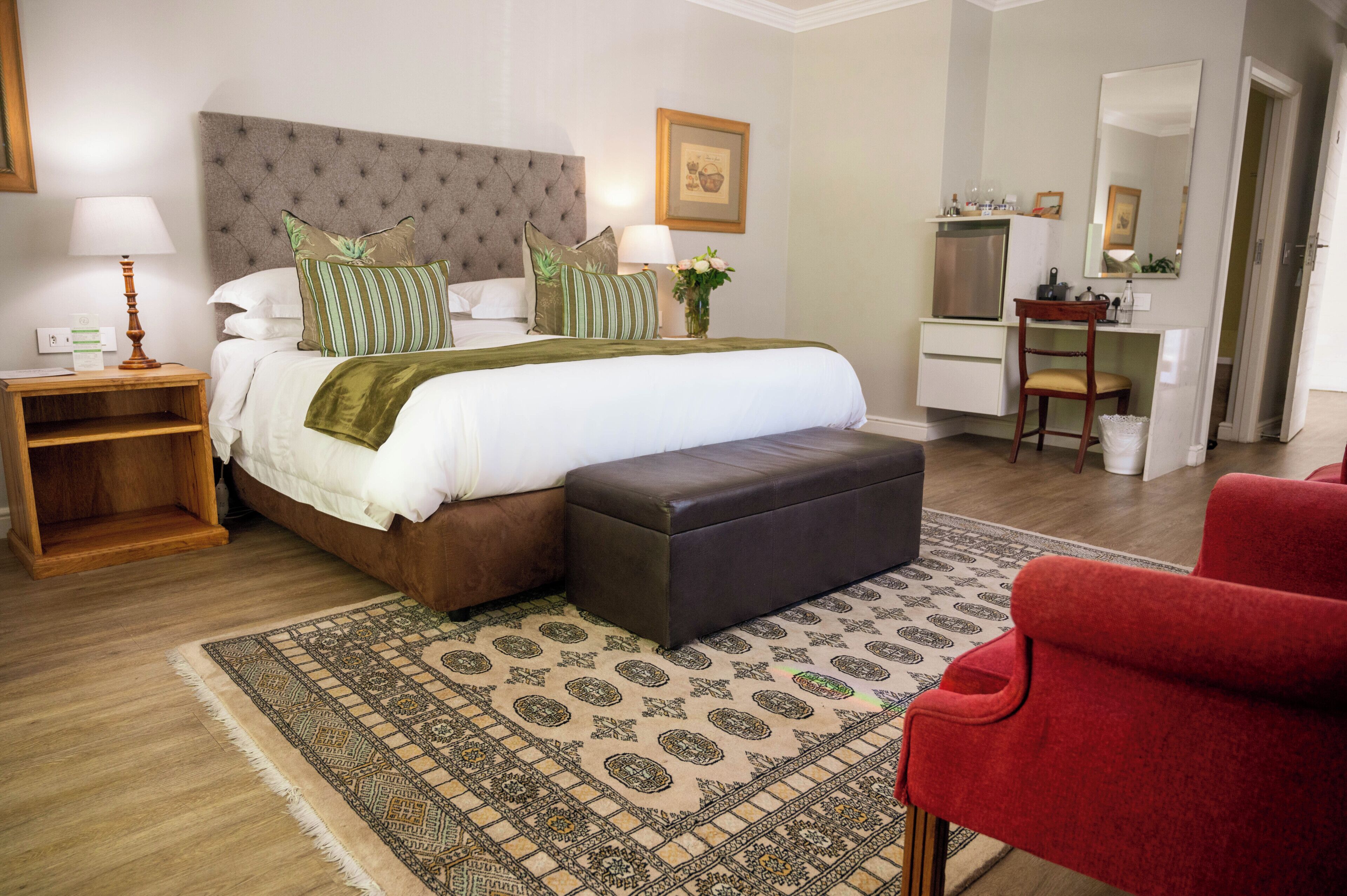 A hotel room with a bed, bedside table, lamp, and a red chair.