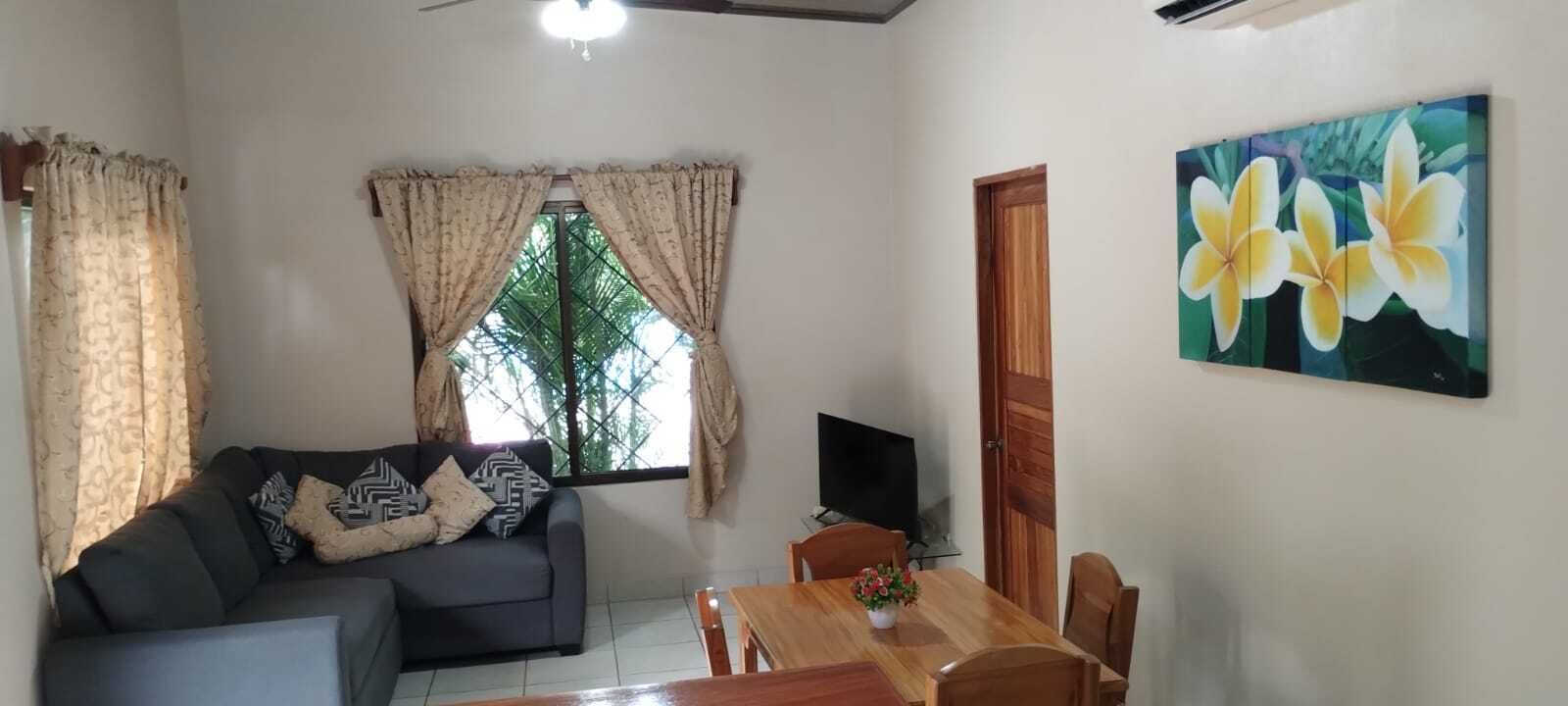 A living room with a sofa, TV, dining table, and a painting of flowers.