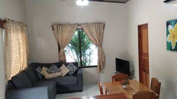 A living room with a sofa, TV, dining table, and a painting of flowers.
