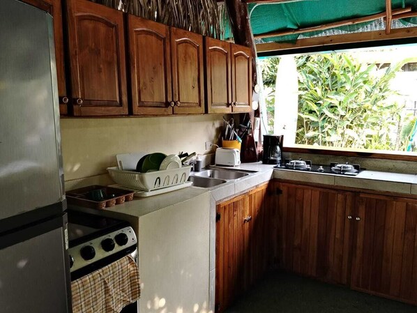Une cuisine compacte avec des meubles en bois, un réfrigérateur en acier inoxydable, une cuisinière et une fenêtre donnant sur un espace verdoyant.
