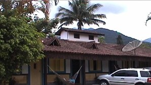 A house with a satellite dish, a car parked in front, and a palm tree in the background. - Patricio's Chalés (Ilhabela)