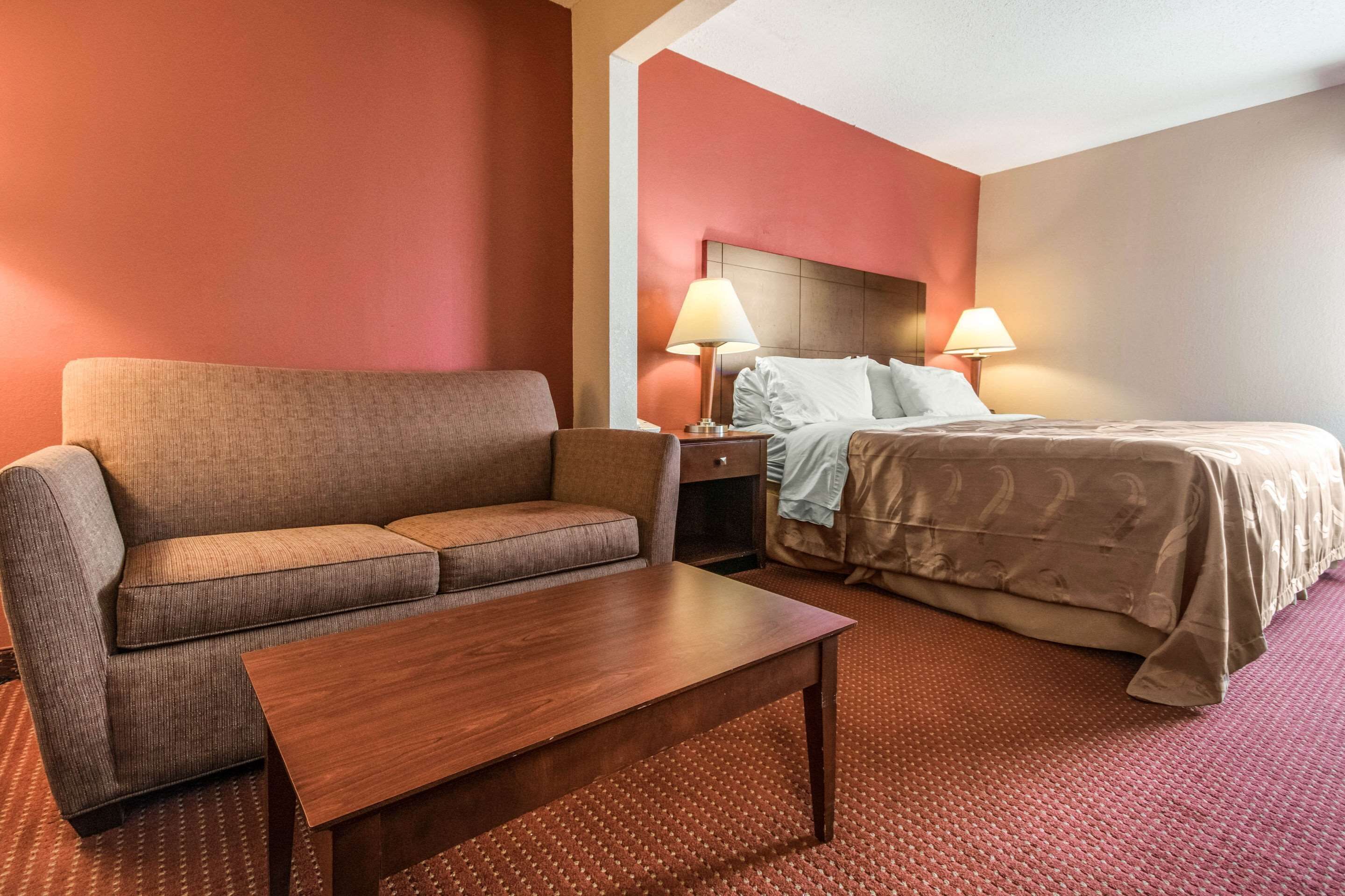 Une chambre d’hôtel avec un canapé, un lit, une table de chevet et deux lampes.