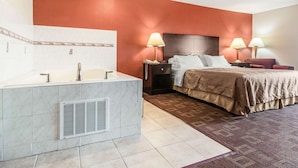 Habitación de hotel con una cama grande, dos mesitas de noche con lámparas, un baño con tocador y lavabo, y una alfombra estampada.
