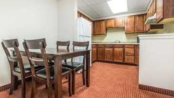 A dining area with a wooden table and chairs, a refrigerator, and wooden cabinets in a kitchen.