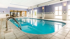 Una piscina interior con suelo de baldosas, una escalera metálica y un borde a cuadros.